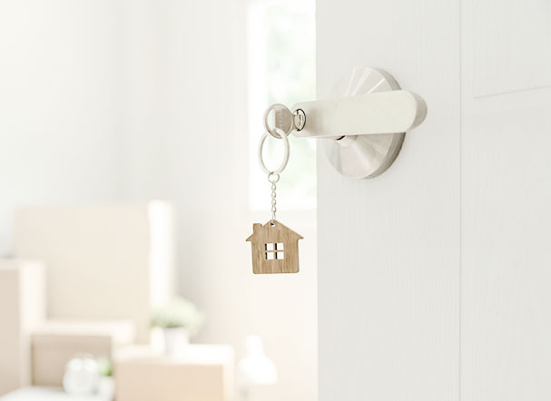 Residential key with a design of a wooden house as a key ring. The key is attached to the door handle