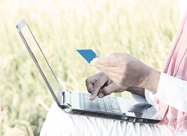 Farmer sitting next to his field, wearing white clothes, using laptop to make online credit card payment