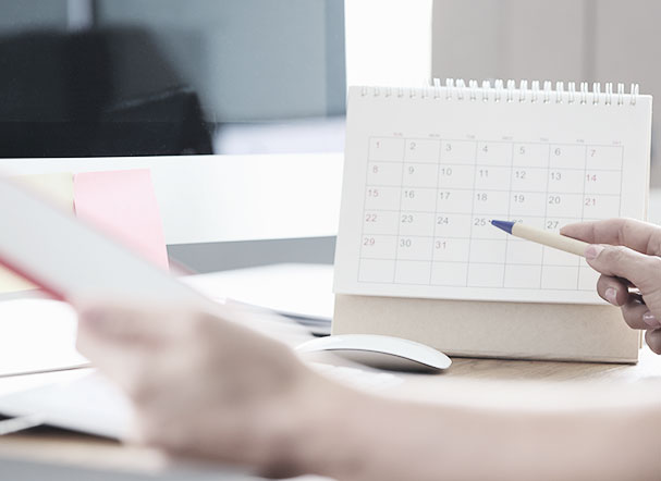Person checking calendar while making notes in notepad