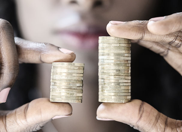 Mulher negra segurando dois montes de moeda. Na mão esquerda, as moedas são em menor número, enquanto na mão direita, são em maior número